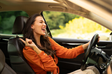 Overjoyed young woman holding auto steering wheel, driving her brand new car and enjoying listening...
