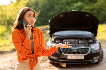 Road accident. Young European woman calling towing service on road, having phone conversation with...