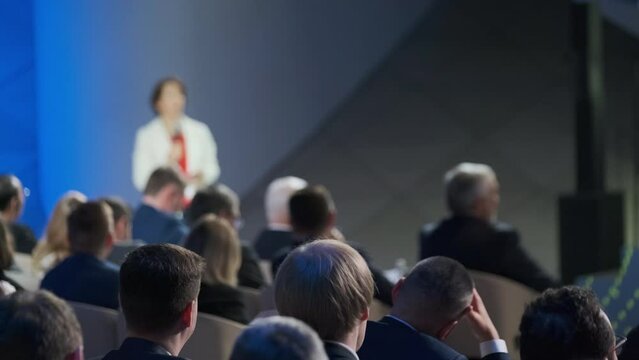 A professional businesswoman delivers a presentation to a diverse audience at a corporate conference. Focus on engagement and leadership in a formal setting.