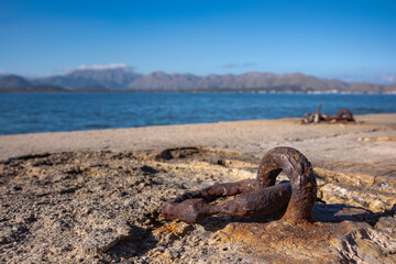 A rusty metal mooring ring has left rusty marks on the concrete in which it is embedded. Remains of dried seaweed hang on the metal