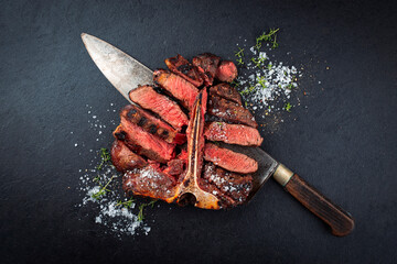 Barbecue dry aged chianina porterhouse beef steak with crystal salt and thyme served as top view on a large butcher knife on a black design board