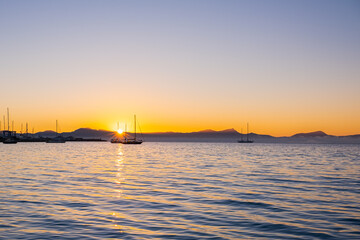 Sea harbor at dawn. The sky, painted golden by the rising sun, is reflected in the calm ripples of the sea. The yachts stand out in beautiful silhouettes against the sky, bathed in the light of dawn