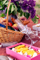 Still life with a basket of lilac flowers, glasses, wine, fruit and croissants. Beautiful picnic close-up picture