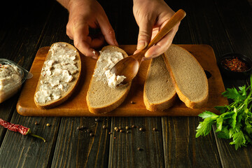 A wooden spoon in the hands of a man for spreading grated lard on rye bread before preparing hearty...