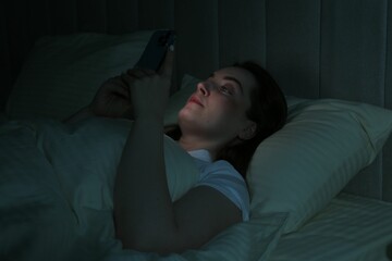Woman using smartphone on bed at night. Internet addiction