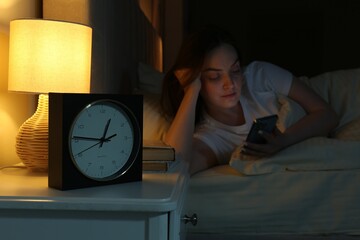 Woman using smartphone on bed at night, selective focus. Internet addiction