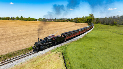 Stunning aerial image of a retro steam train emitting a dark plume of smoke as it travels alongside...