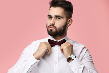 Portrait of handsome man adjusting bow tie on pink background