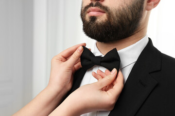 Woman adjusting bow tie to man indoors, closeup