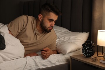 Frustrated man looking at alarm clock on bed