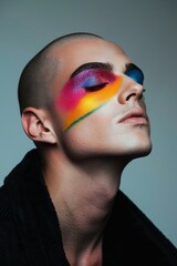 Close up of gay man with funky bright makeup on blue background. Male wearing rainbow colored eyeshadow. Gay lifestyle and LGBT fashion. Beauty, makeup and skin care concept. Design for banner, flyer
