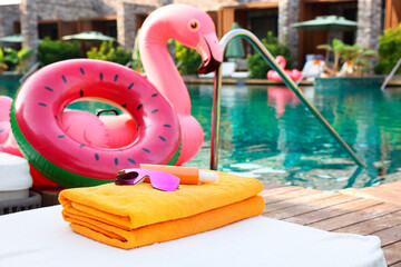 Beach accessories on sun lounger, inflatable ring and float near outdoor swimming pool at luxury...