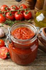Homemade tomato sauce in jar and fresh ingredients on wooden table, closeup