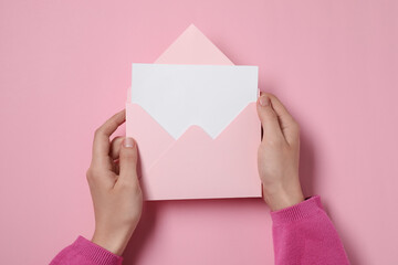 Woman holding letter envelope with card at pink table, top view