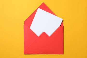 Blank sheet of paper in open letter envelope on orange background, top view