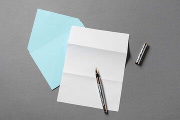 Blank sheet of paper, letter envelope and pen on grey background, top view
