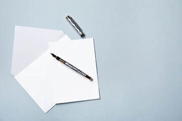 Blank sheet of paper, letter envelope and pen on grey background, top view. Space for text