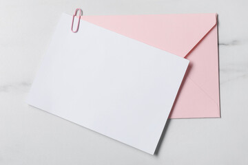 Blank sheet of paper, paperclip and letter envelope on white marble table, top view