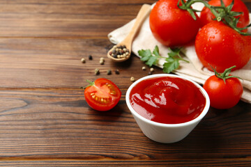Delicious ketchup in bowl and tomatoes on wooden table. Space for text