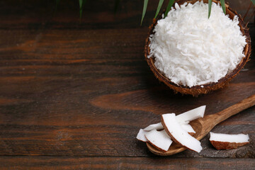 Coconut flakes, spoon and nut on wooden table, space for text