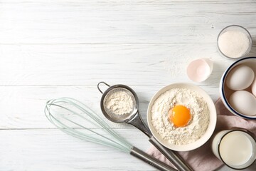 Flour with yolk in bowl and other ingredients for dough on white wooden table, flat lay. Space for text