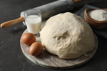 Raw dough, rolling pin and ingredients on black table