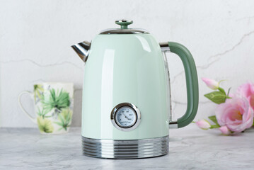 Fancy green electric kettle in with thermometer stands on table with cup and roses.