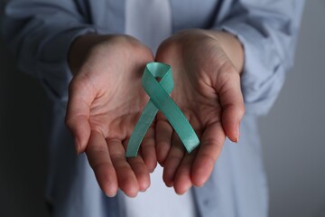 Woman holding turquoise awareness ribbon on grey background, closeup