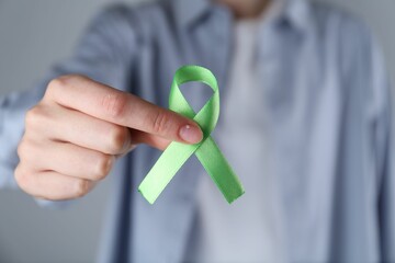 Woman with green awareness ribbon on grey background, closeup