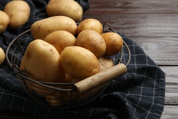 Raw fresh potatoes in metal basket on wooden table, closeup