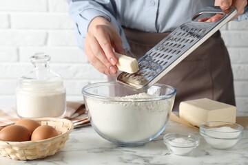 Woman grating butter into bowl with flour at white marble table, closeup