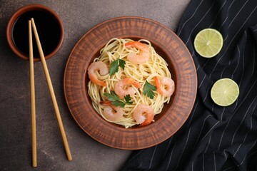 Tasty spaghetti with shrimps, parsley, lime and soy sauce on brown table, flat lay