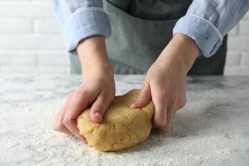 Making shortcrust pastry. Woman kneading raw dough at white marble table, closeup
