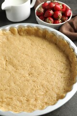 Making shortcrust pastry. Raw dough in baking dish, strawberries and milk on grey table