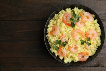 Delicious risotto with shrimps and parsley in bowl on wooden table, top view. Space for text