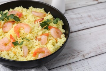 Delicious risotto with shrimps and parsley in bowl on white wooden table, closeup. Space for text
