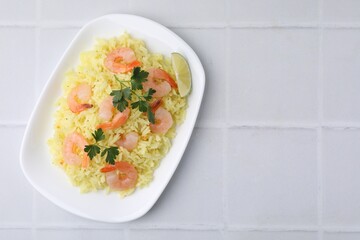 Delicious risotto with shrimps, lime and parsley on white tiled table, top view. Space for text