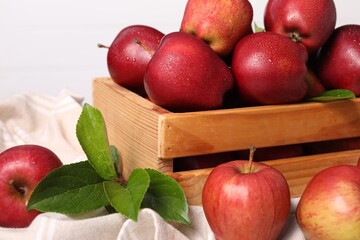 Fresh red apples and leaves in wooden crate on table, closeup