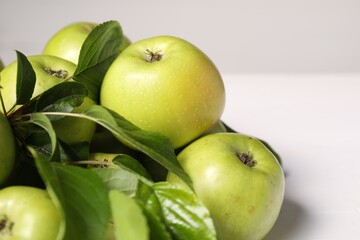 Fresh ripe green apples with leaves on white table, closeup. Space for text