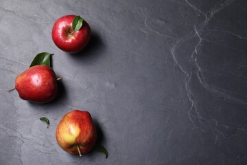 Ripe red apples and leaves on black textured table, flat lay. Space for text