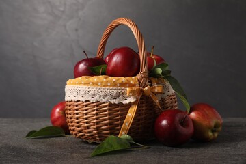 Ripe red apples and leaves in wicker basket on dark grey table