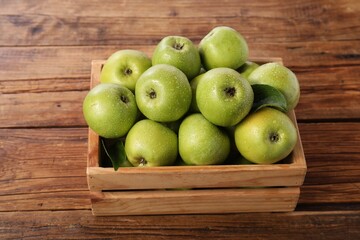 Fresh ripe green apples with water drops in crate on wooden table