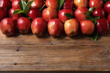 Fresh ripe red apples and leaves on wooden table. Space for text