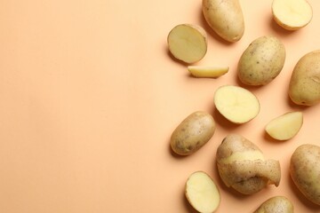Fresh raw potatoes on pale orange background, flat lay. Space for text