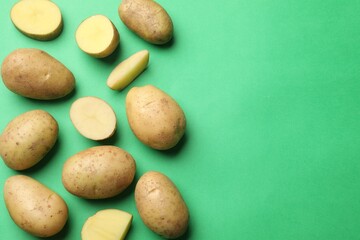 Fresh raw potatoes on green background, flat lay. Space for text