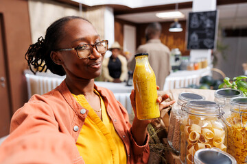 A young black woman films herself in a zero-waste shop promoting eco friendly grocery shopping. She...