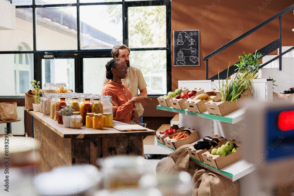 Wall mural Portrait of caucasian boyfriend and african american girlfriend using shopping basket to purchase fresh fruits and vegetables. Smiling multiracial clients in local grocery shop buying organic produce.