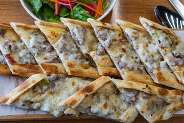 Turkish pita with minced meat. Turkish pizza with minced meat pide and a bowl of salad on a brown table.