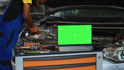 Close up shot of laptop placed on working bench in busy garage next to professional tools while...
