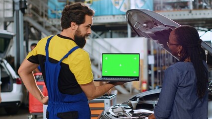 Trained serviceman using green screen laptop in car service to show customer parts needed for...